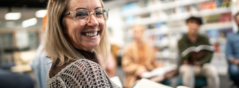 Een vrouw leest een boek en kijkt lachend om.